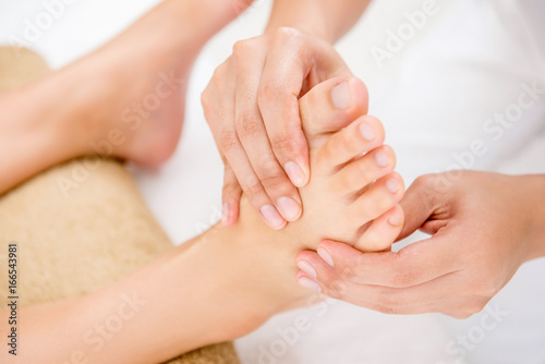 Therapist giving relaxing thai reflexology foot massage to a woman in spa