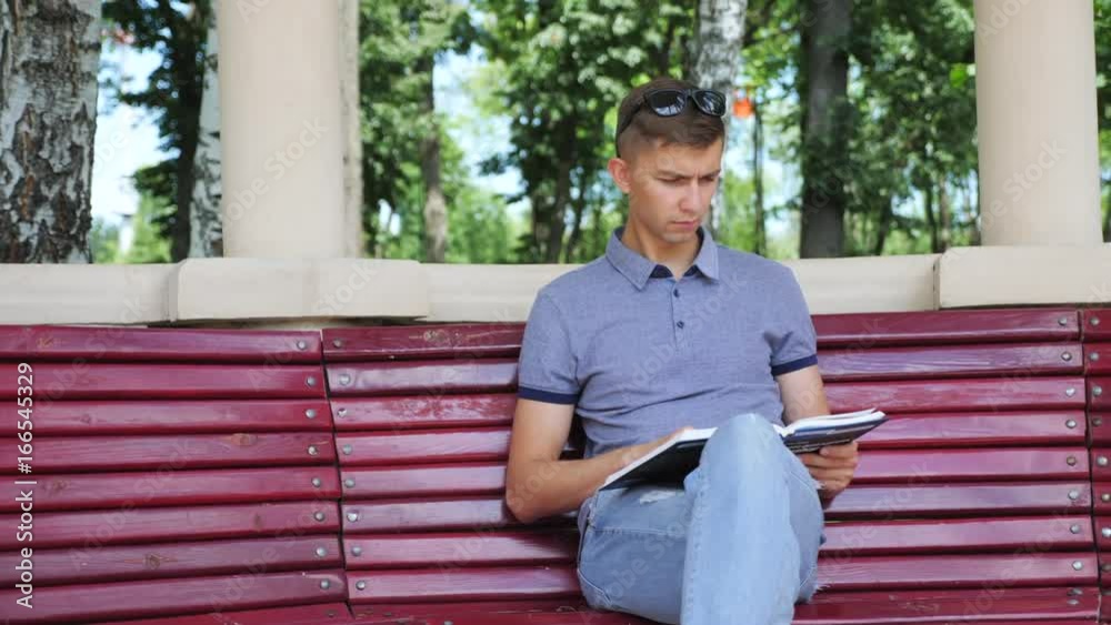 Reading Book In the Park. Young man reading a book in the park sitting on a bench in an arch with columns Reading Book In the Park. Young man reading a book in the park sitting on a bench in an arch with columns