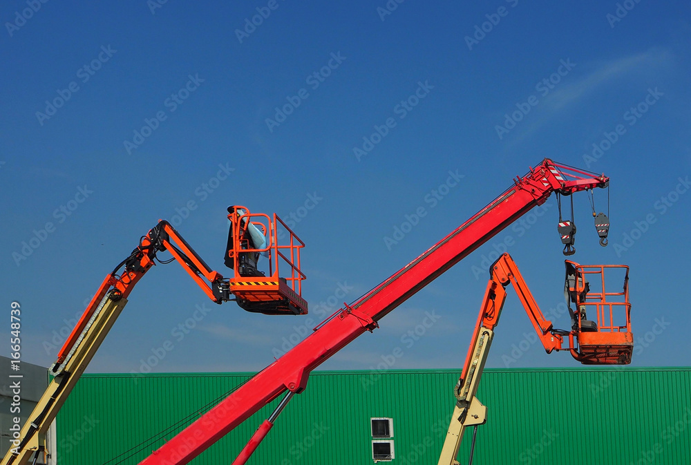 Telescopic crane and two aerial platforms of cherry pickers in a construction site under a blue sky Telescopic crane and two aerial platforms of cherry pickers in a construction site under a blue sky