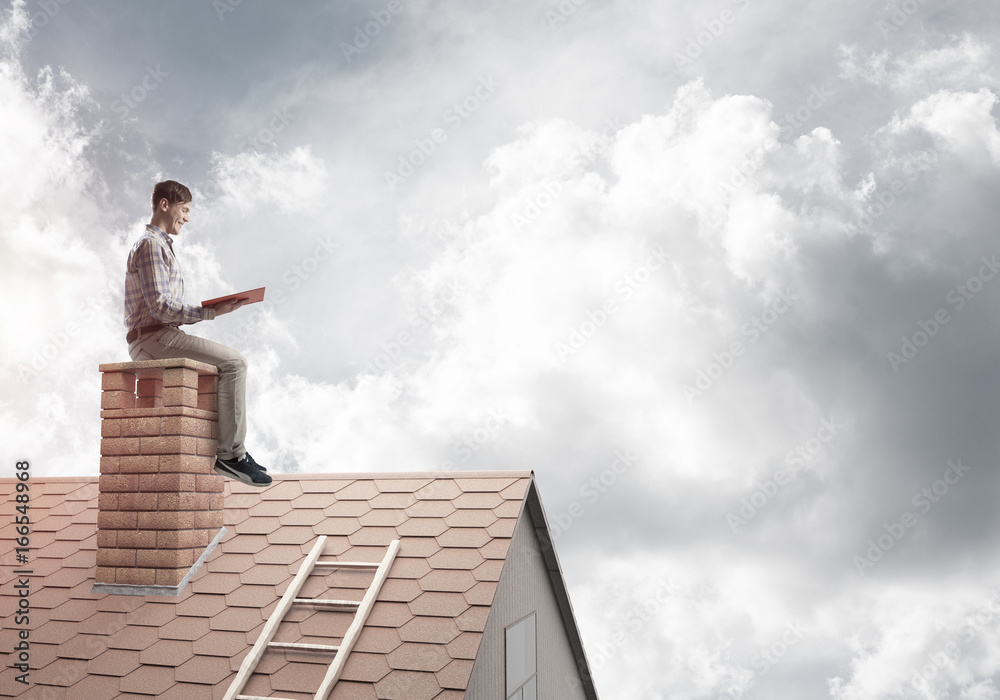 Handsome man on brick roof against cloud scape reading book Handsome man on brick roof against cloud scape reading book
