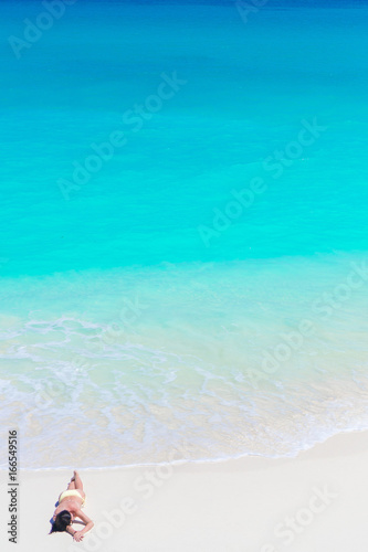 Top view of young beautiful girl lying on the beach at shallow tropical water