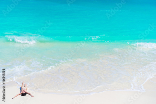 Top view of young beautiful girl lying on the beach at shallow tropical water on the seashore