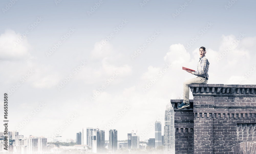 Man on roof edge reading book and cityscape at background Man on roof edge reading book and cityscape at background