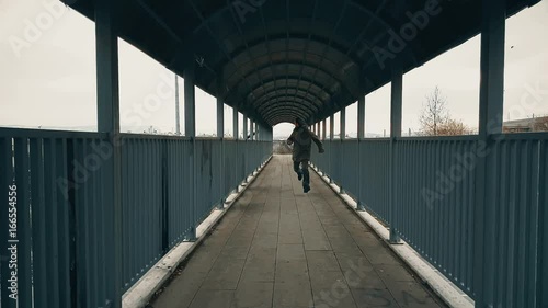 Man running away through the footbridge towards the camera over highway