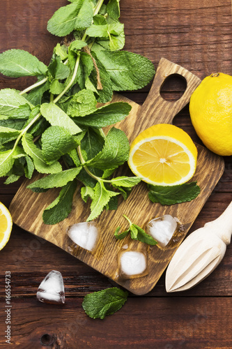 Fototapeta Naklejka Na Ścianę i Meble -  Ingredients for lemonade - lemon, mint, ice on a wooden cutting board on a wooden background