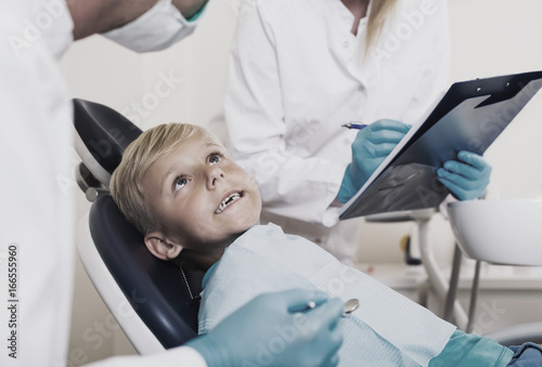 Male dentist with female assistant are diagnosticating to young patient which is sitting