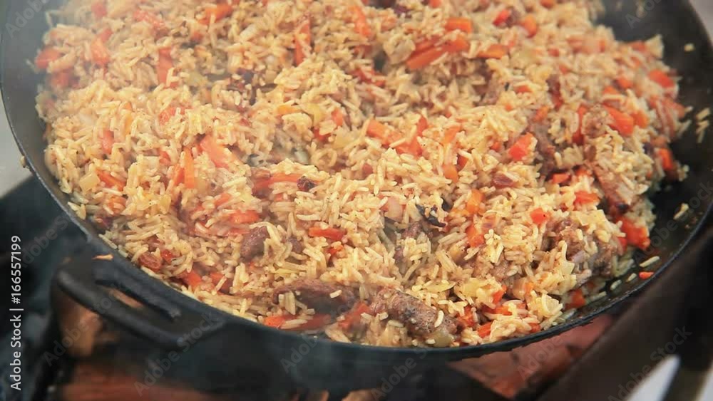 A huge bowl of pilaf (Middle East traditional food of rice and meat) cooks on the open fire A huge bowl of pilaf (Middle East traditional food of rice and meat) cooks on the open fire