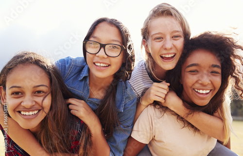 Four teenage girls having fun piggybacking outdoors photo