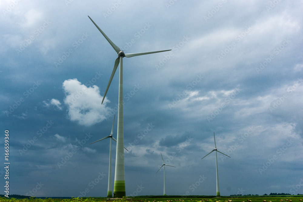 Fototapeta premium Wind Turbines and green fields with hay rolls on a cloudy day. Near storm