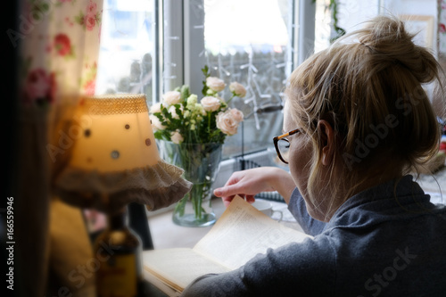 beautiful young woman reading interesting book while drinking tea at home, in cafe