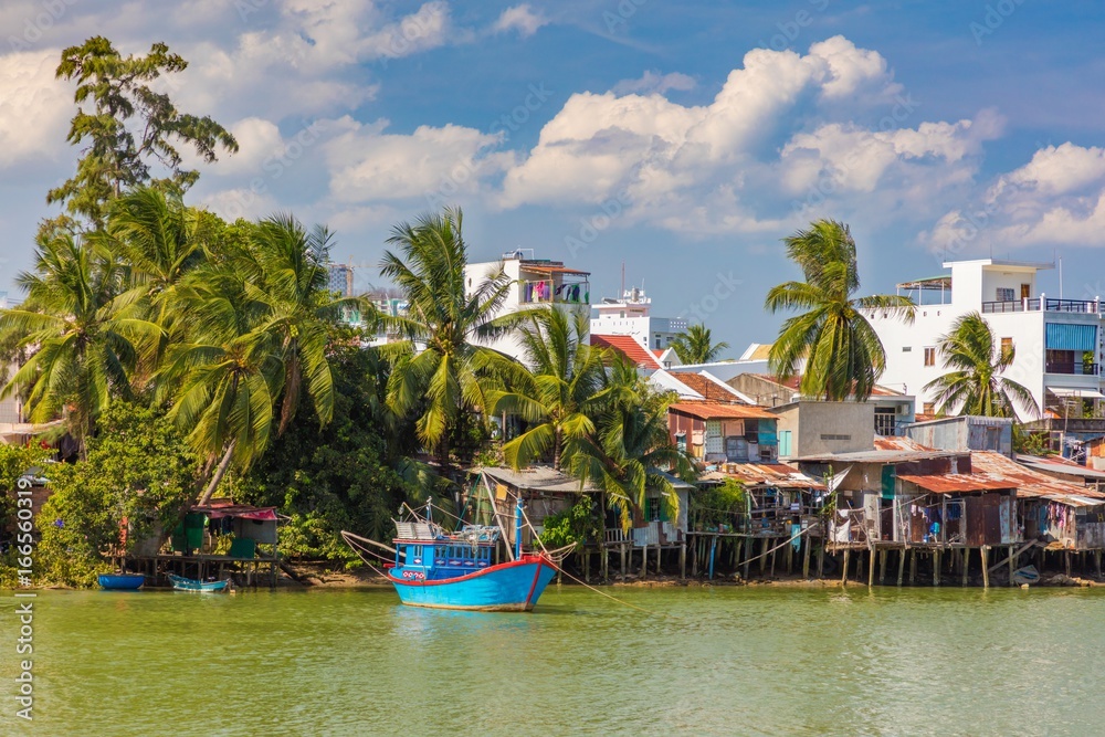 A Vietnamese fishing boat on the Cai river in Nha Trang central Vietnam. With palm trees and houses lining the riverbank. Asia.