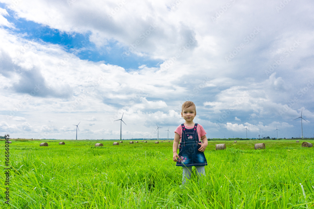 little cute caucasian girl looking forward concept at wind power generator turbine in background