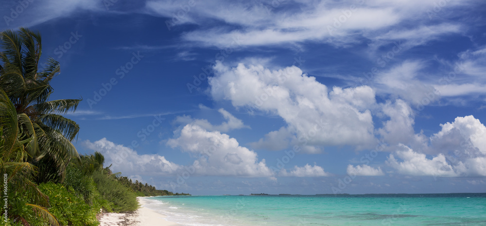 Panoramic view of Maldivian tropical beach with bright sea water under blue sky and white clouds on background