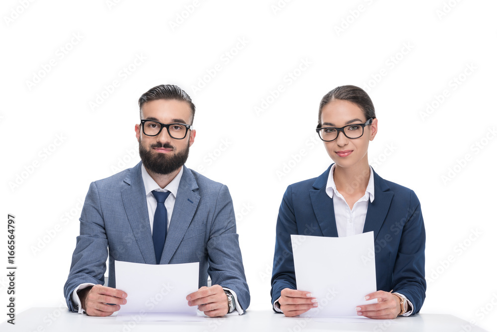 two newscasters with papers sitting at table and looking at camera, isolated on white two newscasters with papers sitting at table and looking at camera, isolated on white