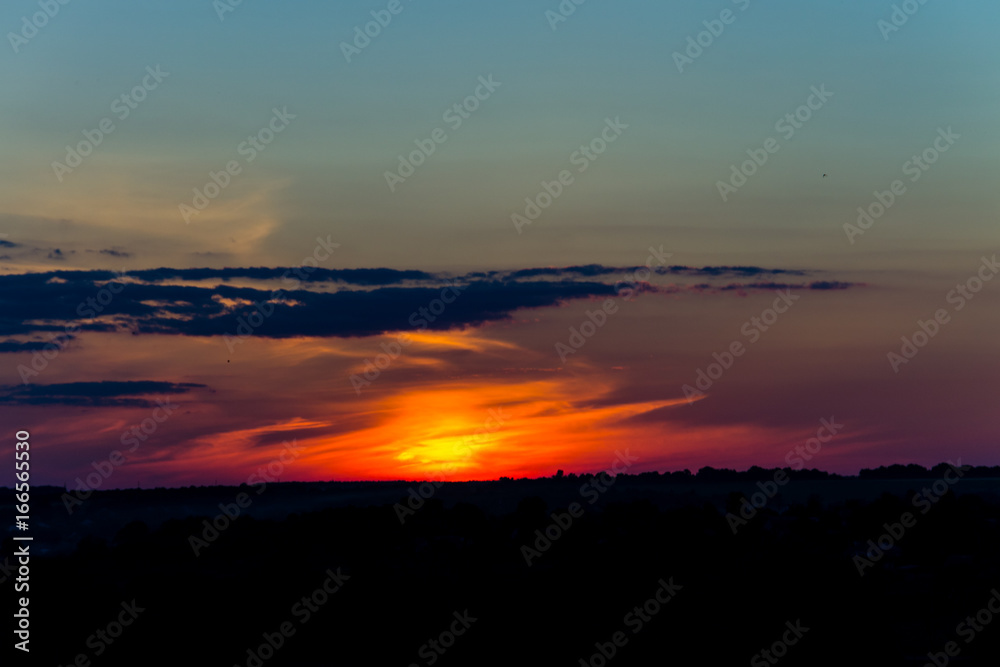 Orange sunset over silhouettes of village and trees