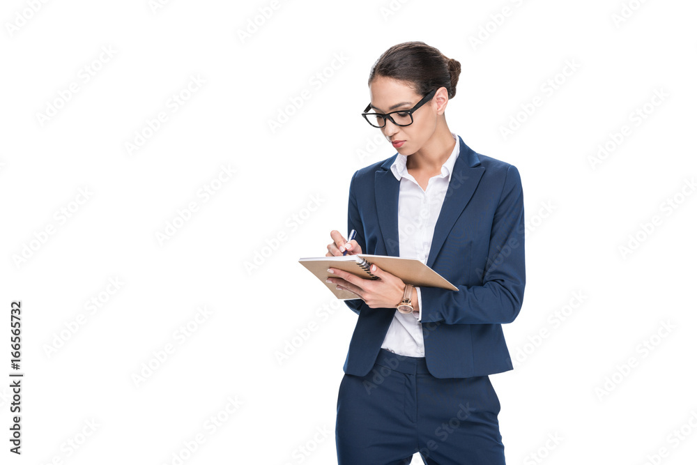 beautiful concentrated businesswoman in suit writing in diary, isolated on white