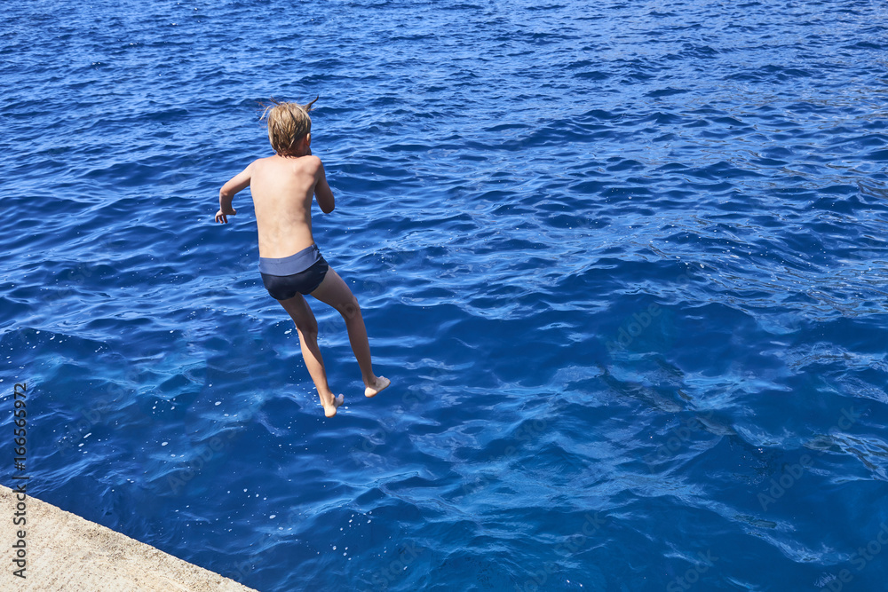 The child boy is jumping into the blue sea