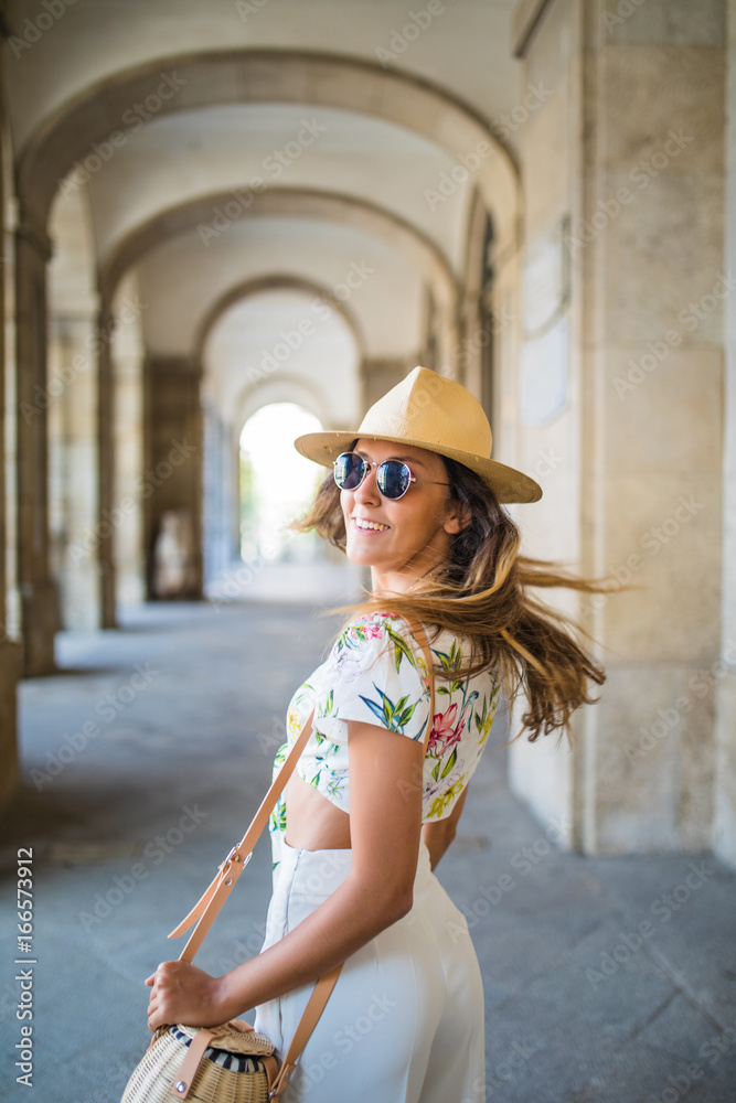 Beautiful brunette young woman wearing hat and sunglasses and walking on the street summer time
