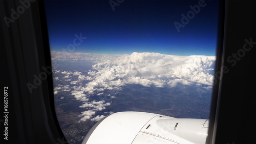 Flying in a airplane over the clouds. View from plane aircraft passenger window to the wing.