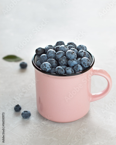 Fresh blueberries in pink cup on light gray stone background. photo