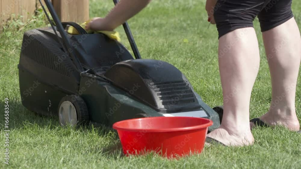 Woman cleaning and maintaining lawn mower after mowing grass in the backyard Woman cleaning and maintaining lawn mower after mowing grass in the backyard
