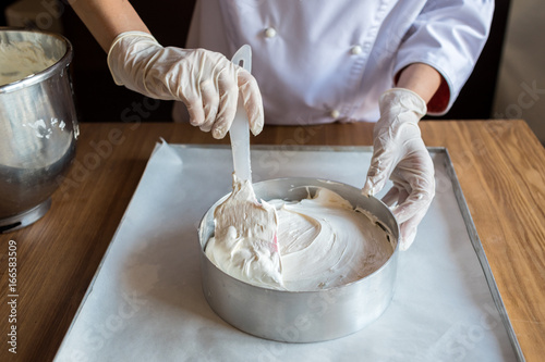 Female chef cook in rubber gloves preparing vanilla cake-mix dough in form for baking cake. Young woman baker pouring the dough in baking dish