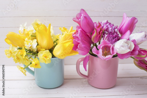 Bright yellow  and pink spring   flowers in cups on white  wooden background.