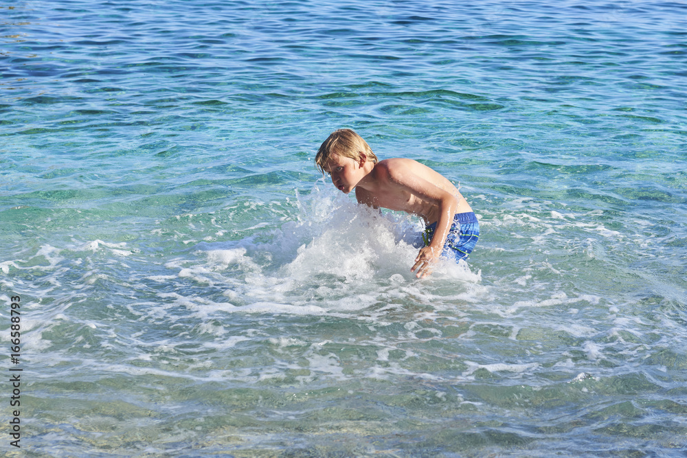 handsome child boy splashes water on the azure sea. Children playing in azure sea. Concept of vacations and recreation at sea handsome child boy splashes water on the azure sea. Children playing in azure sea. Concept of vacations and recreation at sea