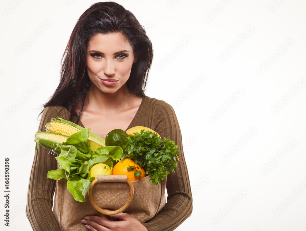 Happy young woman holding a paper shopping bag full of vegetable food Happy young woman holding a paper shopping bag full of vegetable food