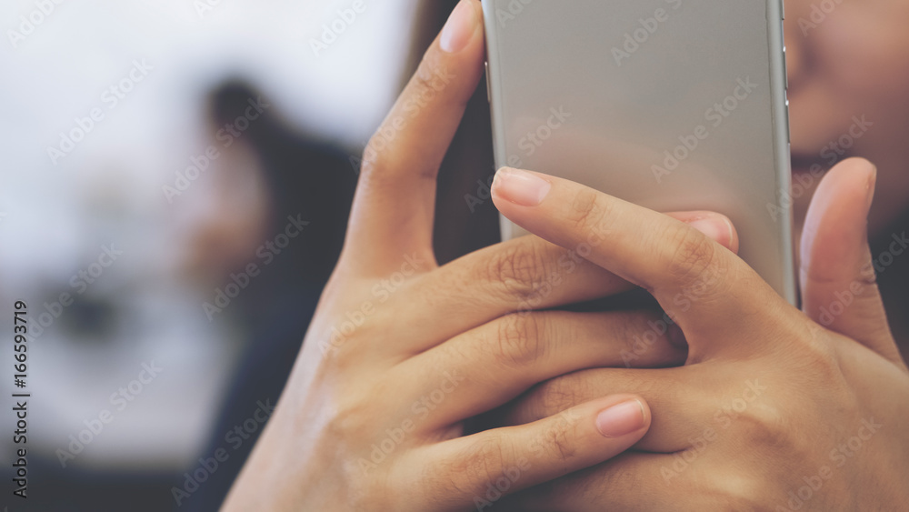Closeup image of an Asian woman holding , using and looking at smart phone with blur background