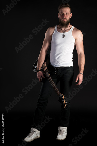 KIEV  UKRAINE - May 03  2017. A charismatic and stylish man with a beard holds an electric guitar in his hand on a black isolated background. Vertical frame