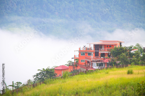  A beautiful sunshine morning. A orange color building in the golden meadow. Background is forest with mist.