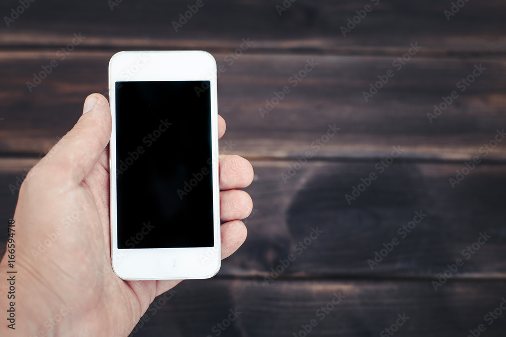 Smartphone in hand over wooden table. Empty copy space screen mockup.