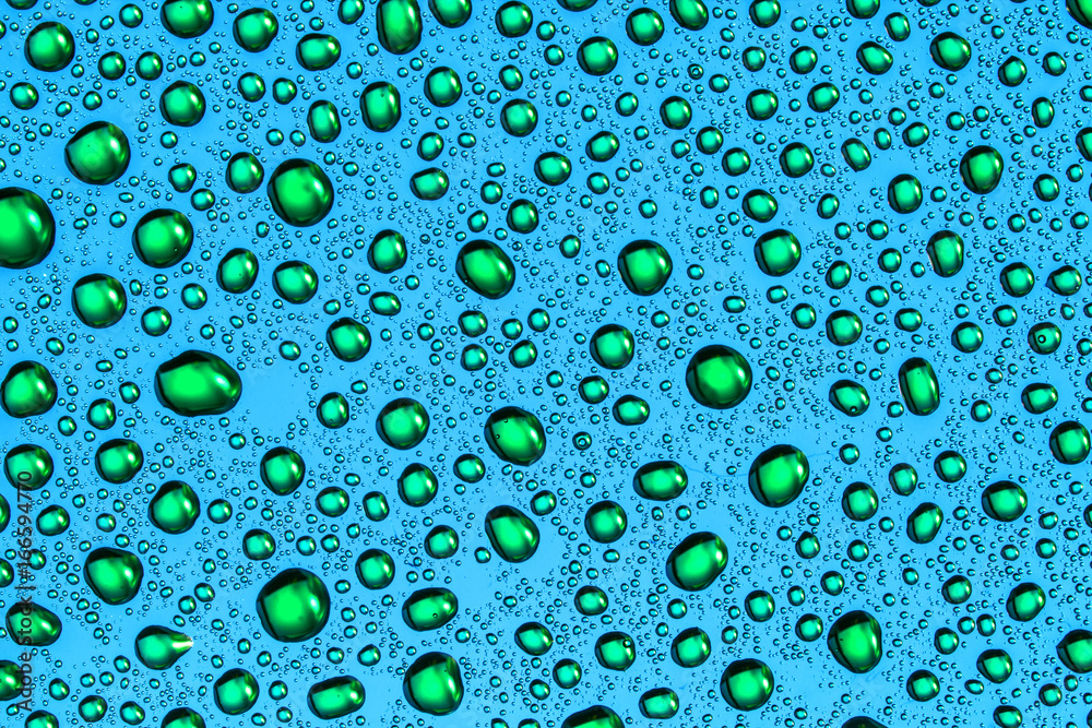 Green water drops on blue bright glass surface pattern background.