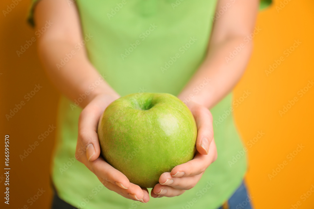 Young woman holding green apple in hands on color background, closeup Young woman holding green apple in hands on color background, closeup