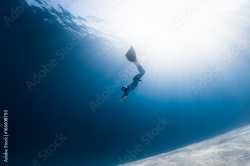 Woman freediver glides over sandy bottom in a tropical clear sea with sun rays