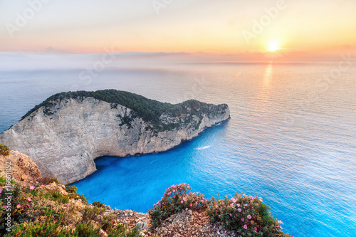 Sunset scenery with sun disc falling behind Ionian sea at Navagio beach with shipwreck view, Zakynthos - Zante island in Greece. Very popular and famous travel destination for summer vacations.