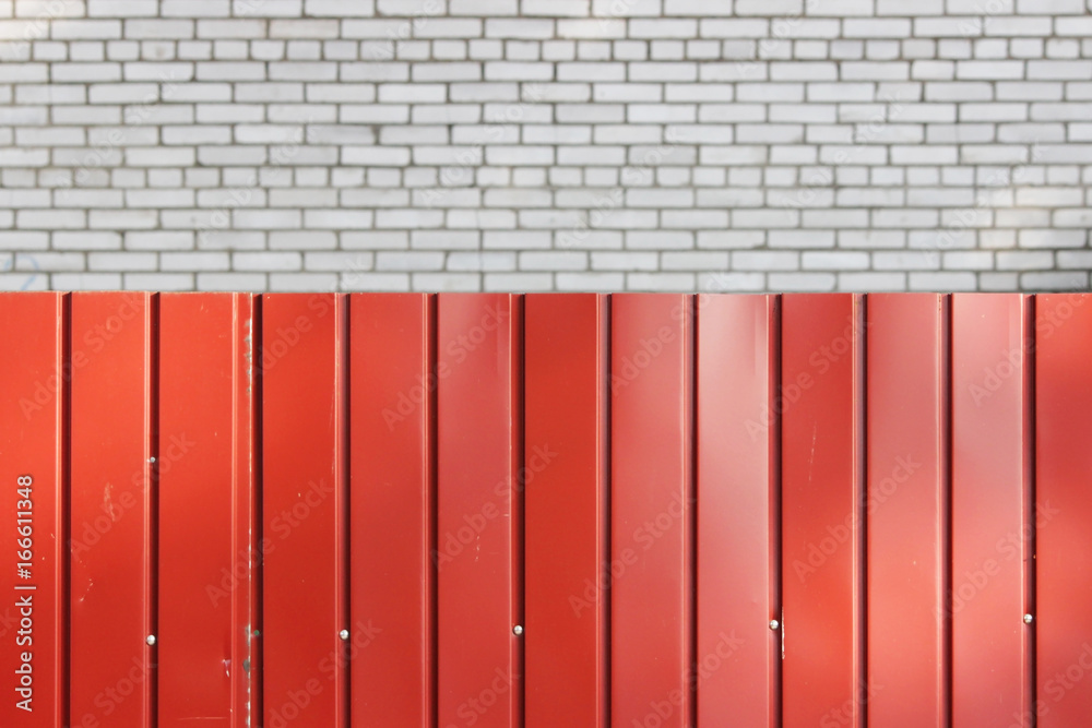 Red gate made of metal siding against the brick wall of the house.