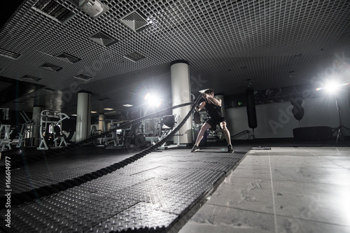 Fitness man working out with battle ropes at gym. Battle ropes fitness man at gym workout exercise fitted body. Fitness man training with battle rope in fitness club. Training with battle rope photo