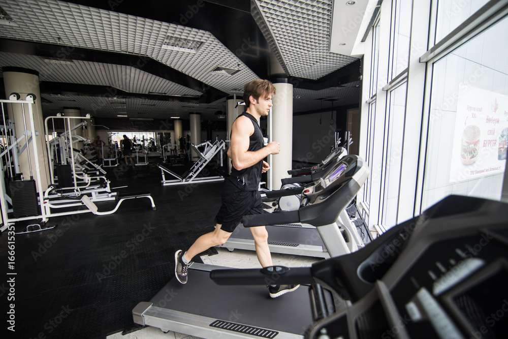 Young man in sportswear running on treadmill at gym. side view Young man in sportswear running on treadmill at gym. side view