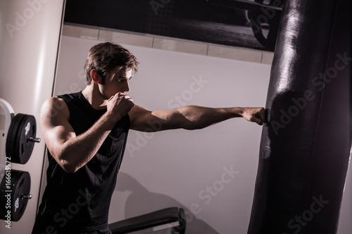 Concentrated muscular kickbox fighter exercising with punch bag on white in gym photo