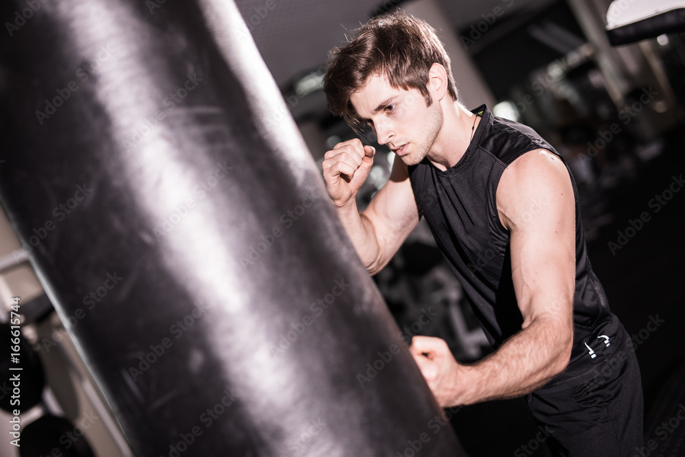 Portrait of boxer trying to kicking punching bag in gym while training. Training