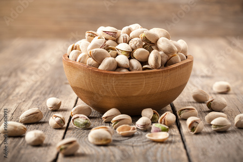 Pistachio nuts in a wooden bowl on wooden table
