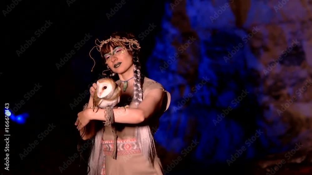 Fairy woman in medieval clothes strokes an owl in a cave Fairy woman in medieval clothes strokes an owl in a cave