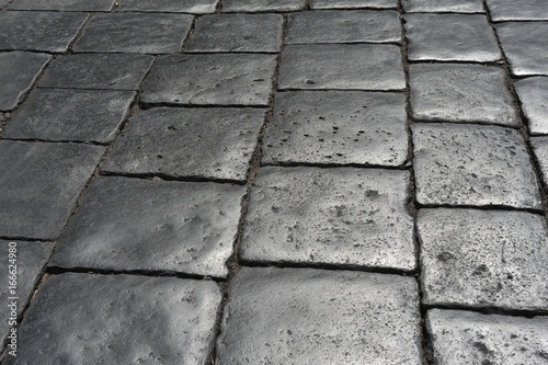 Oberfläche/Hintergrund: Historisches, durch den Verkehr glattgeschliffenes Straßen-Pflaster aus großen Basalt-Steinen in der Stadt Syracus, Sizilien, Italien. Stein aus Lava des nahen Vulkans Ätna