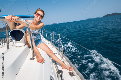 Happy young woman sits on deck of the boat sailing in the tropical sea