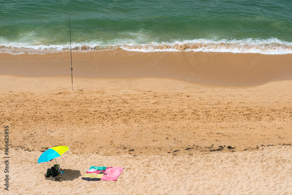 Summer view from above of sun parasols and a fishing rod on a sunny beach in Portugal. Summer view from above of sun parasols and a fishing rod on a sunny beach in Portugal.