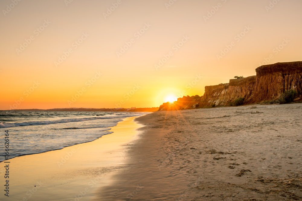 Beautiful colorful sunset in Algarve Portugal. Peaceful beach water and cliffs.
