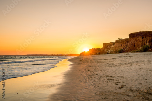 Beautiful colorful sunset in Algarve Portugal. Peaceful beach water and cliffs.