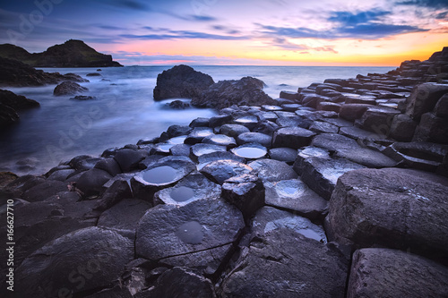 sunset over basalt rocks formation Giant's Causeway, Port Ganny Bay and Great Stookan, County Antrim, Northern Ireland, UK photo